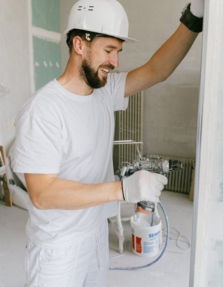 A happy construction worker using a drill indoors during renovation.