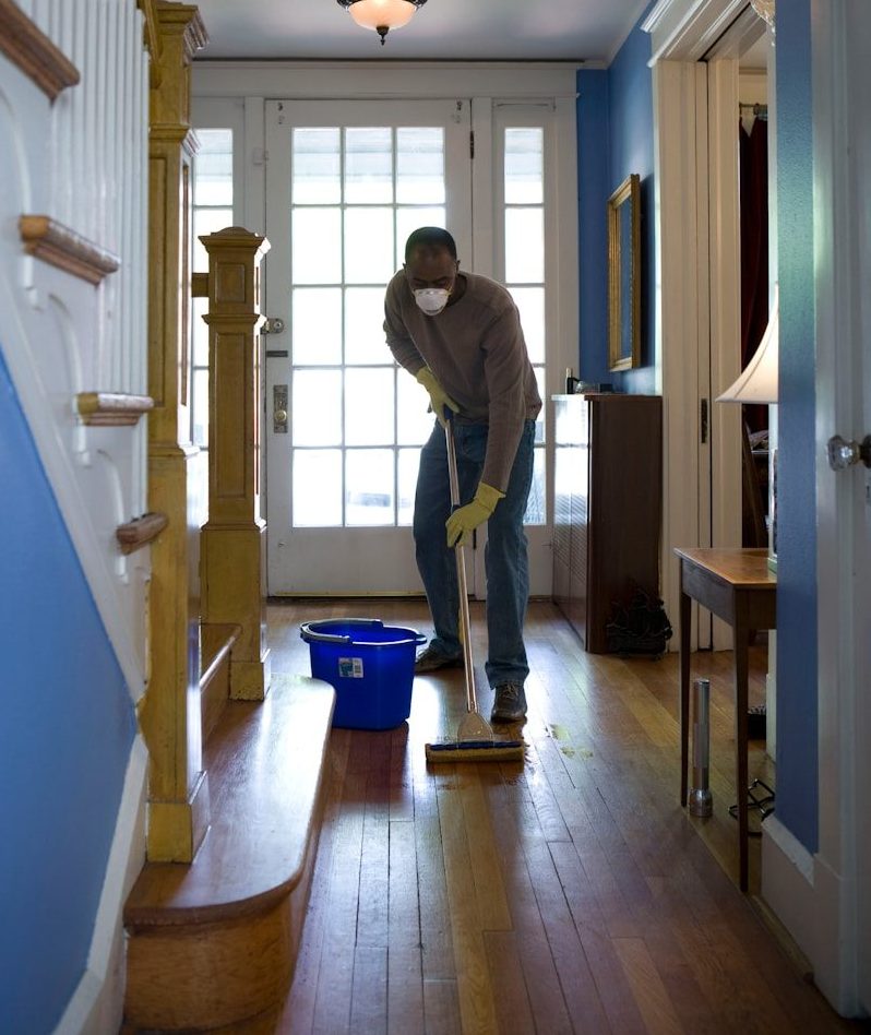 man in gray hoodie and blue denim jeans standing on brown wooden parquet flooring